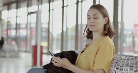 Pretty female using smart phone on bench in airport terminal and walking to Stock Footage 134652445