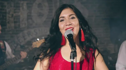 Pretty female vocalist sings into microphone on stage with musical group Stock Footage 105164553