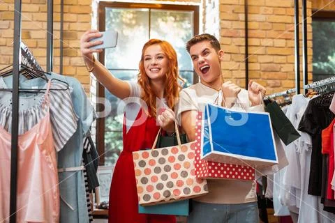 Pretty girl and her emotional boyfriend smiling and taking selfies in clothes Stock Photos