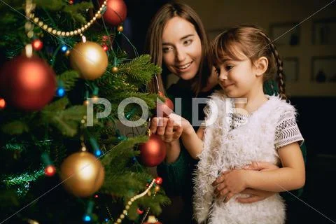 Pretty girl and her mother looking at one of decorative xmas bubbles on firtree Stock Photos