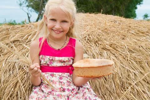 Pretty girl with bread sitting on a haystack. Stock Photos