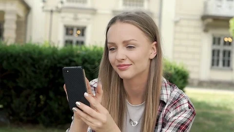 Pretty girl browsing internet on smartphone while sitting in the park, steadycam Stock-Footage 79295341