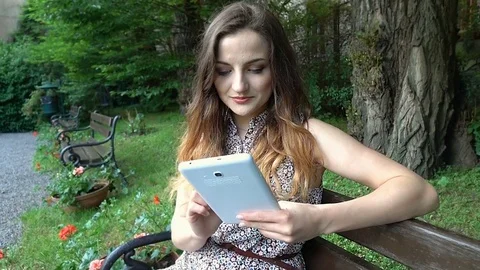 Pretty girl browsing internet on tablet in the park and smiling to the camera Stock Footage 76991375