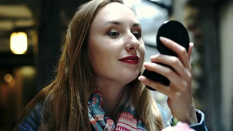 Pretty girl checking her appearance in the mirror while sitting in the cafe Stock Footage