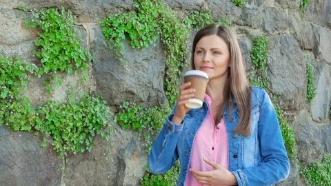 Pretty girl in a cotton jacket drinking coffee against the background of a wall Stock Footage 77065064