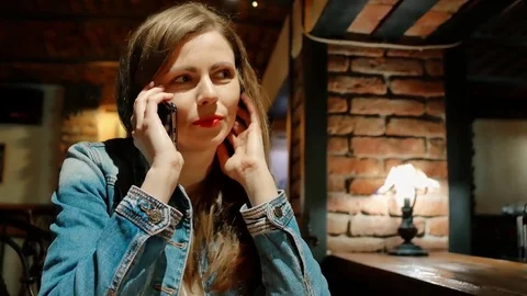 Pretty girl in a cotton jacket talking on smartphone in a cafe. Vintage interior Stock Footage