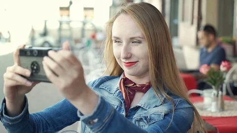 Pretty girl in denim jakcet sitting in the outdoor cafe and doing selfies on old Stock Footage