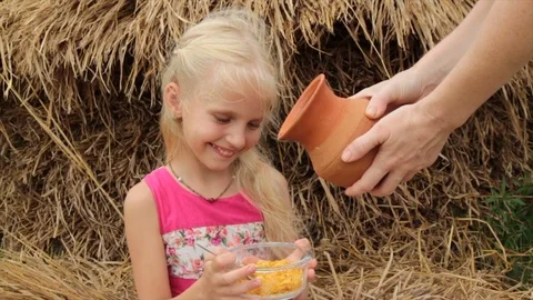 Pretty girl eats corn flakes with milk from a glass jar in a village Video stock 76729131