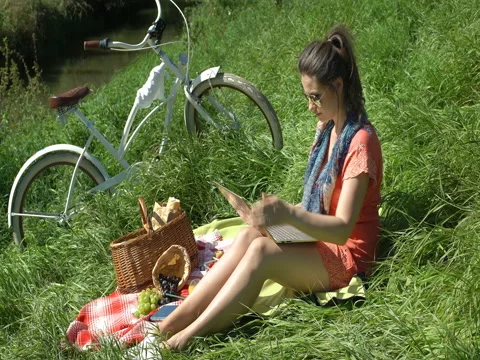 Pretty girl having a picnic on countryside and using modern notebook, steadycam Stock Footage