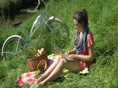Pretty girl holding modern notebook while sitting on the blanket and smiling to Stock Footage