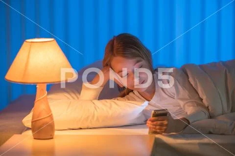The pretty girl lay on the bed and phone. Evening night time Stock Photos