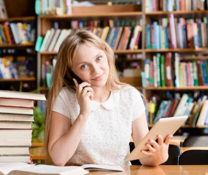 Pretty girl in library using tablet computer and talking on the phone Stock Photos