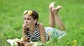 Pretty girl lies on green grass and uses red smartphone HD Footage
