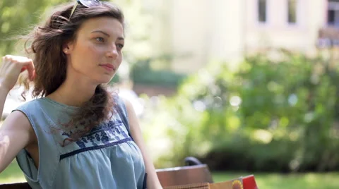 Pretty girl looking thoughtful while sitting on the bench in the park Video stock 67564554
