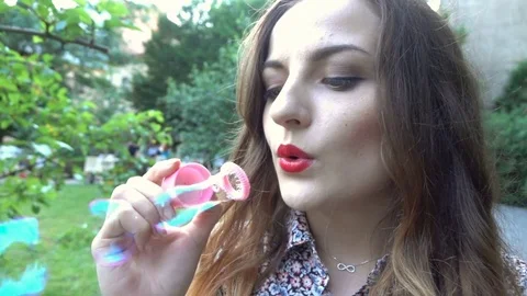 Pretty girl making soap bubbles in the park, steadycam shot, slow motion shot at Stock Footage 76987482