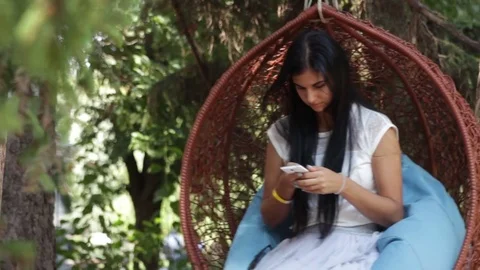 Pretty girl in park on swing, using smartphone Stock Footage