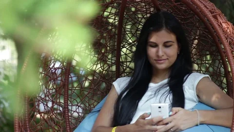 Pretty girl in park on swing, using smartphone Stock Footage 78236314