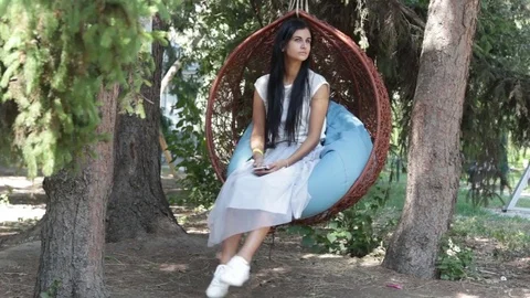 Pretty girl in park on swing, using on smartphone Stock Footage 78238905