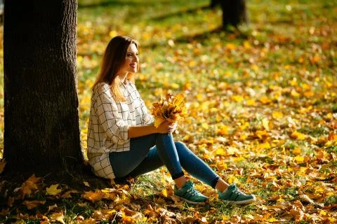 Pretty girl posing while sitting under the tree with a bunch of leaves in her Stock Photos