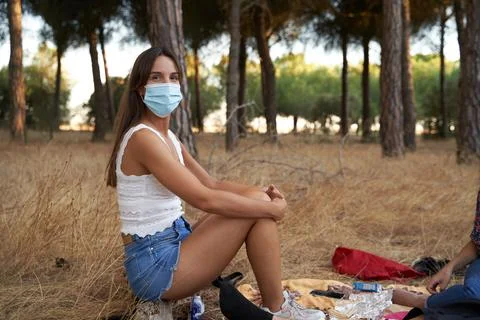 Pretty girl protected with a mask sitting on a tree looking at the camera whi Stock Photos
