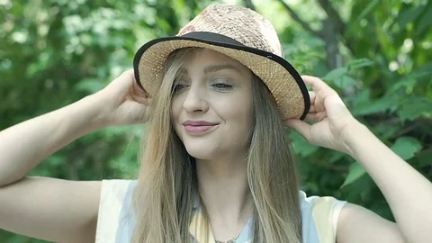 Pretty girl puts on straw hat and looks happy, steadycam shot Stock Footage