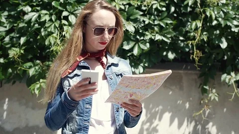 Pretty girl reading map and checking way on smartphone, steadycam shot Stock Footage