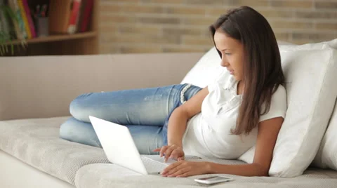 Pretty girl relaxing on couch using laptop looking at camera and smiling Stock Footage 34196856