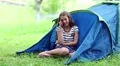 Pretty girl sits on grass near tourist tent and speaks on cell phone HD Footage