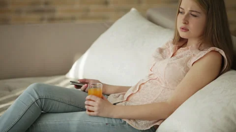 Pretty girl sitting on sofa using mobile phone holding glass of juice  Stock Footage 35440479