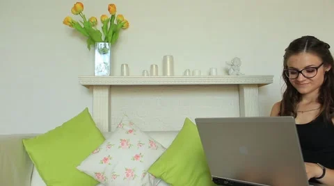 Pretty girl sitting on sofa using laptop and smiling at camera Stock Footage 66359433