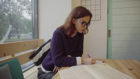 Pretty girl sitting at table studying and writing in notebook Stock Footage 70683340