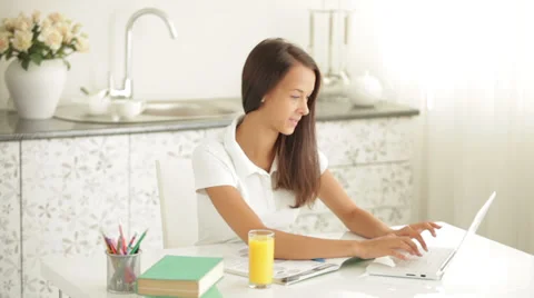 Pretty girl sitting at table using laptop drinking juice and smiling Видео 34196743