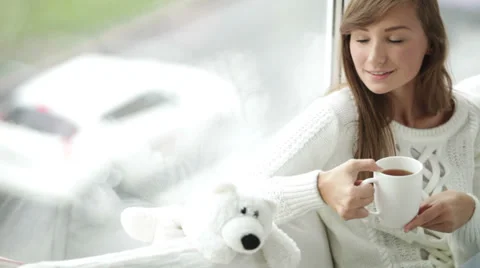 Pretty girl sitting by window drinking tea looking at camera and smiling Video stock 34149998