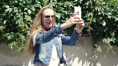 Pretty girl standing outdoors and doing selfies on smartphone, steadycam shot Stock Footage