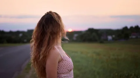 Pretty girl stands at sunset near the road, posing and smiles Stock Footage 80345053