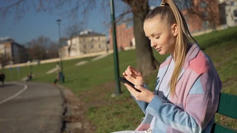 Pretty girl in stylish jacket using smartphone in the park at sunny day, steady 스톡 동영상 70719136