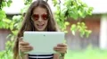 Pretty girl in sunglasses with tablet pc stands under apple tree in garden HD Footage