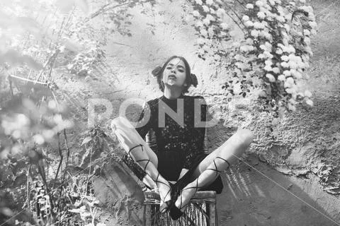 Pretty girl tying shoe laces on wicker chair on sunny day Stock Photos