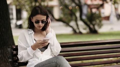 Pretty girl using smartphone while sitting at public space. Cheerful woman Stock Footage 145003561