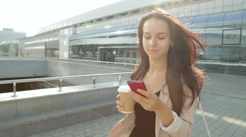 Pretty girl walking and using app on smartphone drinking coffee in the sun Stock Footage 68386323