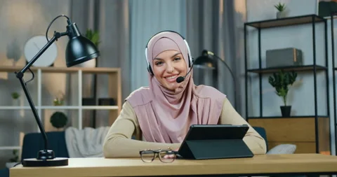 Pretty happy smiling young arabic woman in hijab wears headset sitting at the Stock Footage 150160854
