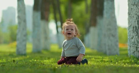 Pretty kid sits on the grass in the park and smiles, happy childhood. Cute blond Stock-Footage 137424847