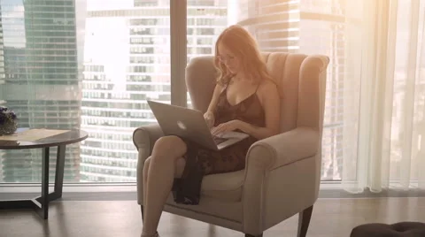 Pretty lady working on her laptop while sitting in an armchair at home Stock Footage 68051758