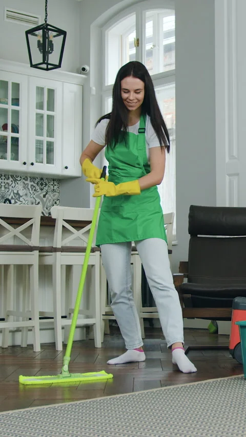 Pretty laughing young amusing female cleaner in green apron washing parquet with Stock Footage 327864191