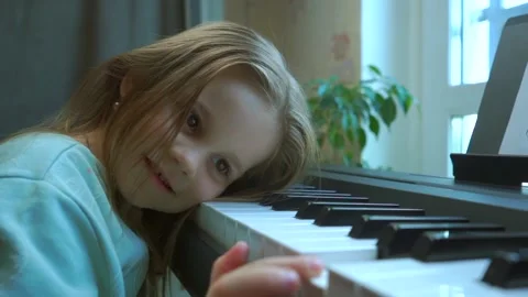 A pretty little girl put her head on the piano keys. Stock Footage
