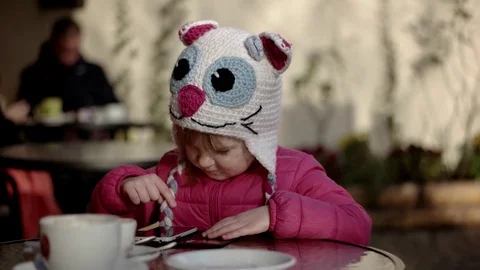 Pretty Little Girl Using App on Smartphone Sits in the Street Terrace 動画素材 71264723