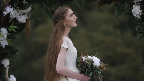 Pretty long haired bride stands under decorated wedding arch Stock Footage 123514985