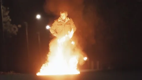 Pretty man in denim jacket uses matches to burn a gas puddle on asphalt Stock Footage 143795415