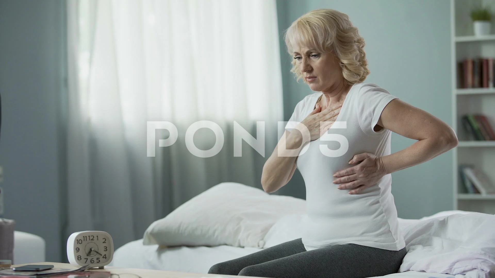 Pretty mature woman sitting on bed and suffering from heart attack, health