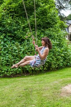 Pretty middle aged dark haired woman swinging on childrens swings Foto stock